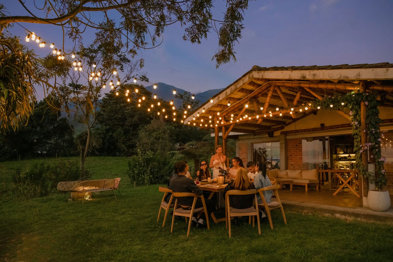 An outdoor family dinner beneath string lights at dusk