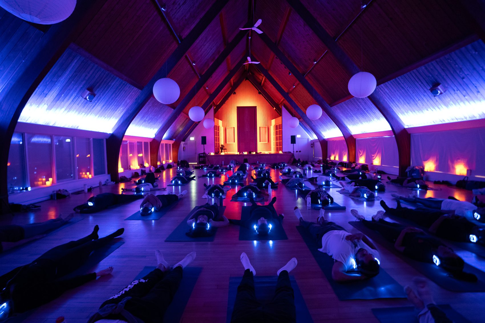 A candlelit hall of Joyride guests resting on mats in glowing headphones
