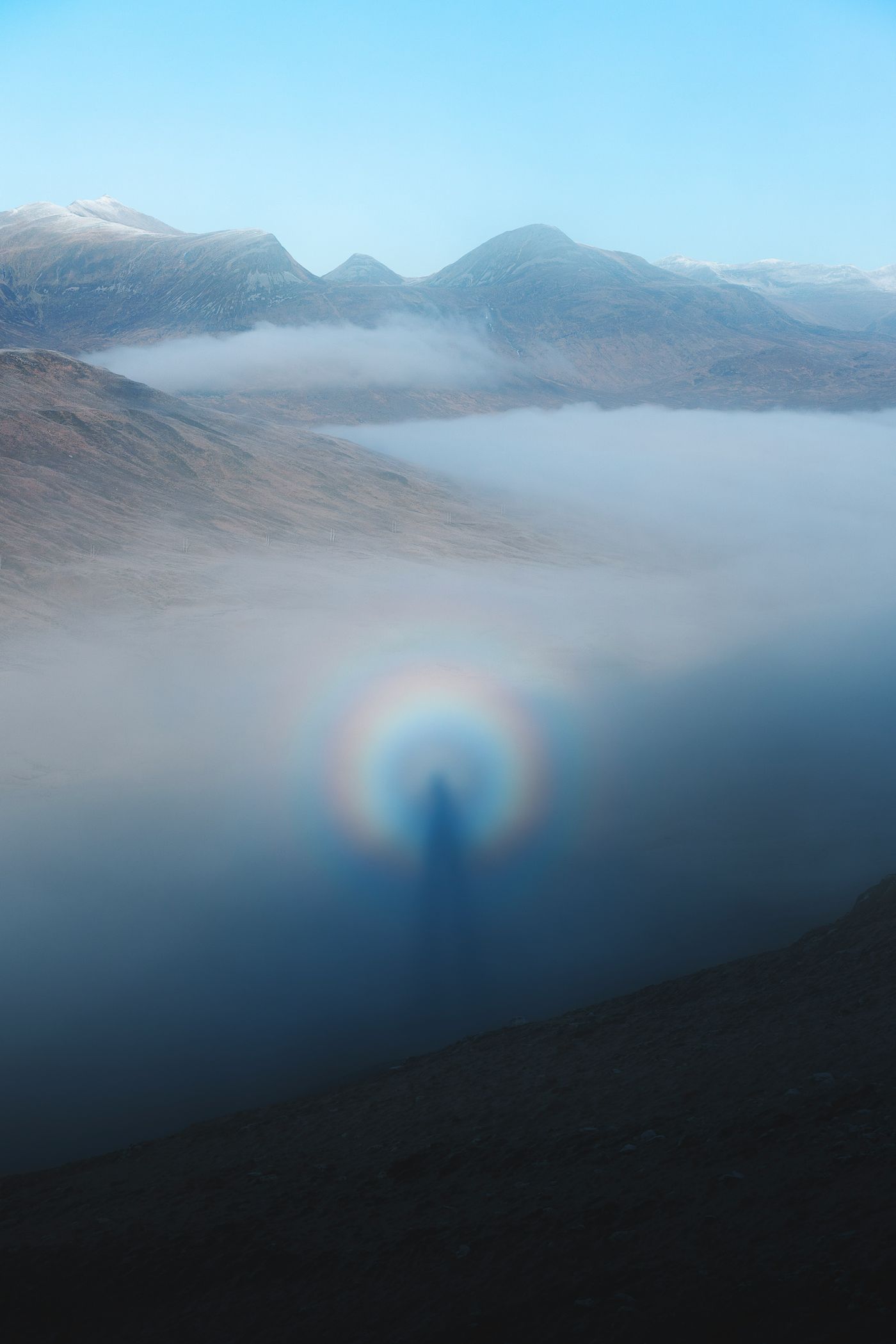 A figure crowned by a circular rainbow above the clouds